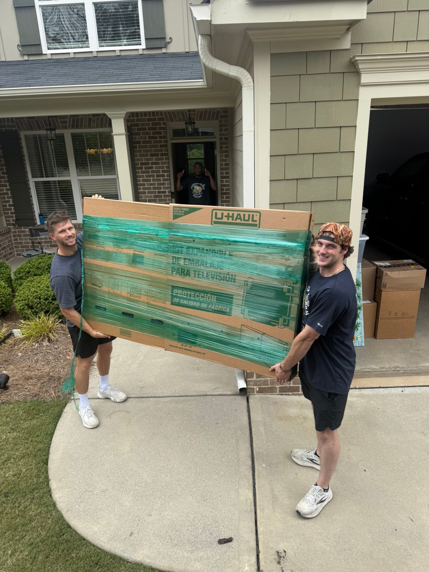 Two-man crew carrying a packed flat-screen TV box from a Greenville-area home