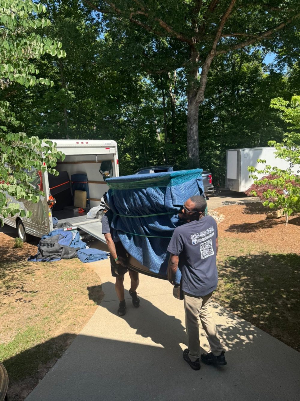 Movers carefully transporting a wrapped mattress out to the truck