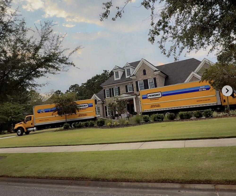 Two Penske moving trucks staged at a large Greenville-area home